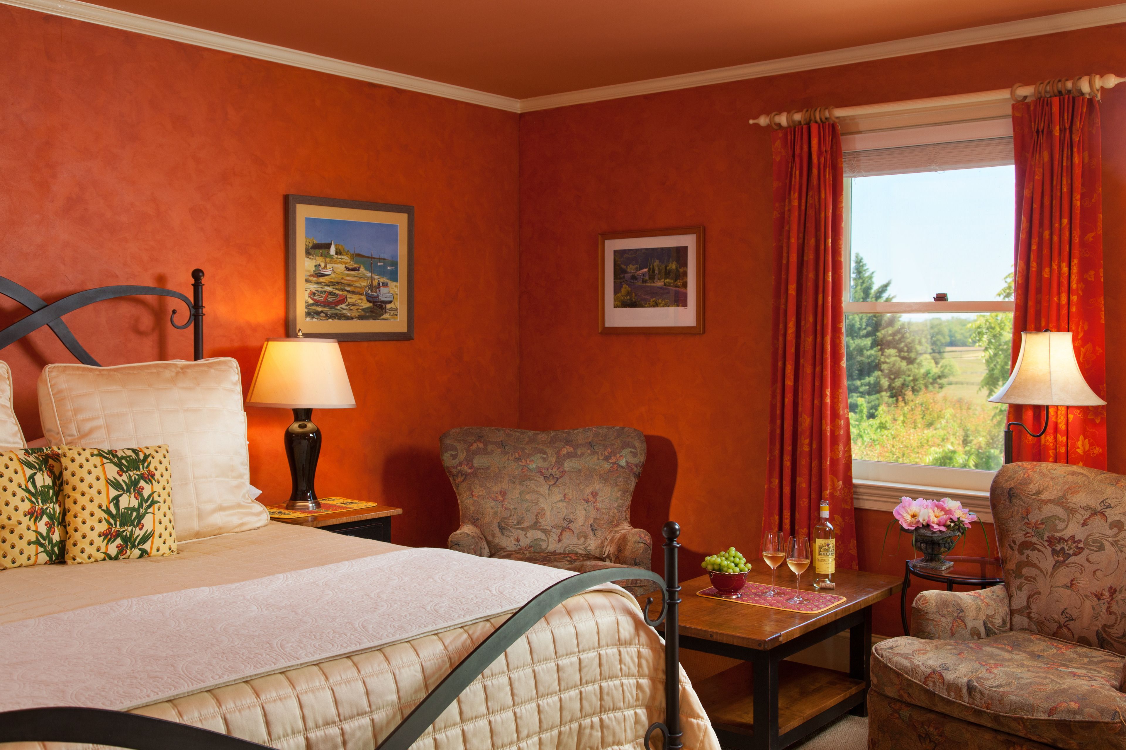 Una habitación de hotel con una cama, dos sillas, una mesa con un florero y una ventana con cortinas.