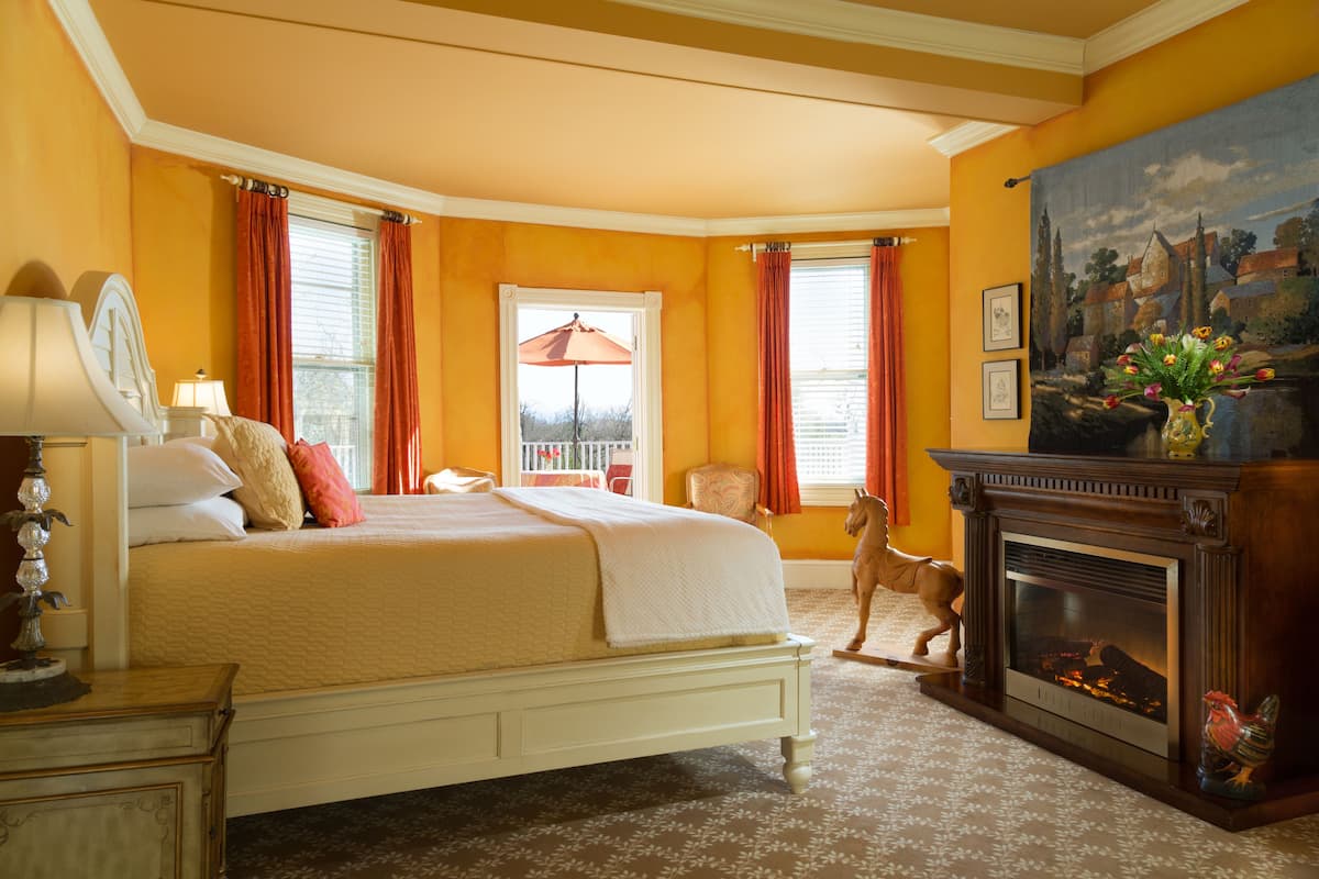 A bedroom with a bed, a fireplace, a window with curtains, and a painting on the wall.