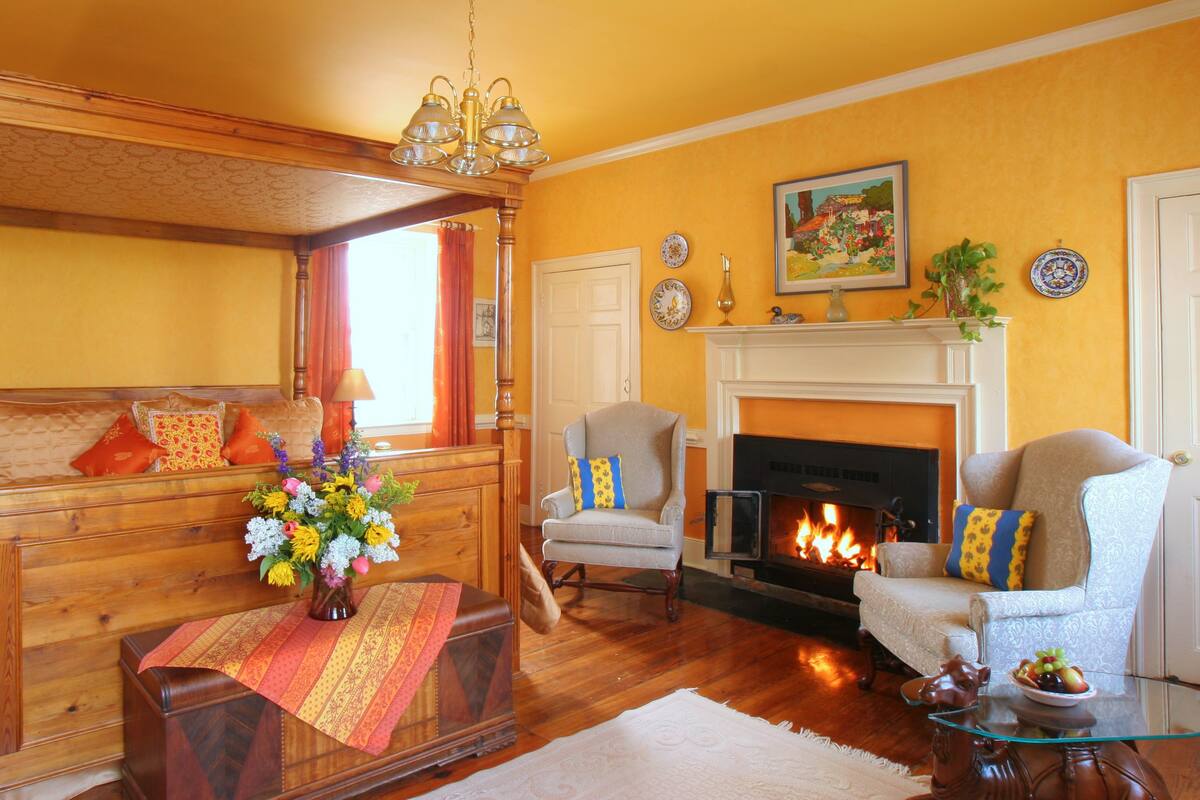 A cozy living room with a wooden sofa, a fireplace, and a large window with curtains.