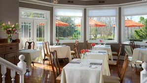A dining area with tables set for service, large windows with views of greenery, and a chandelier. - L'Auberge Provencale Inn & Restaurant (Boyce)
