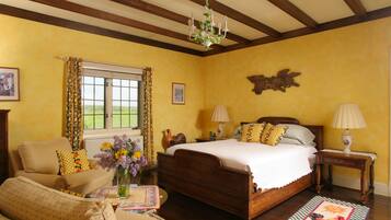 A bedroom with a wooden bed, two bedside tables, a window with curtains, a chandelier, and a view of the outdoors.