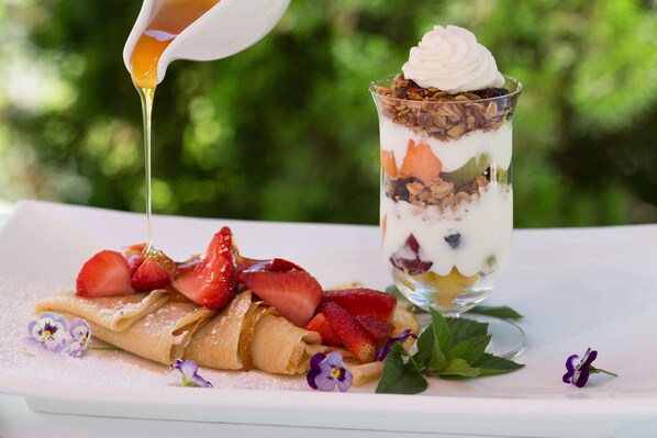 A dessert with a glass container, a plate with rolled pastries, strawberries, and a small flower.