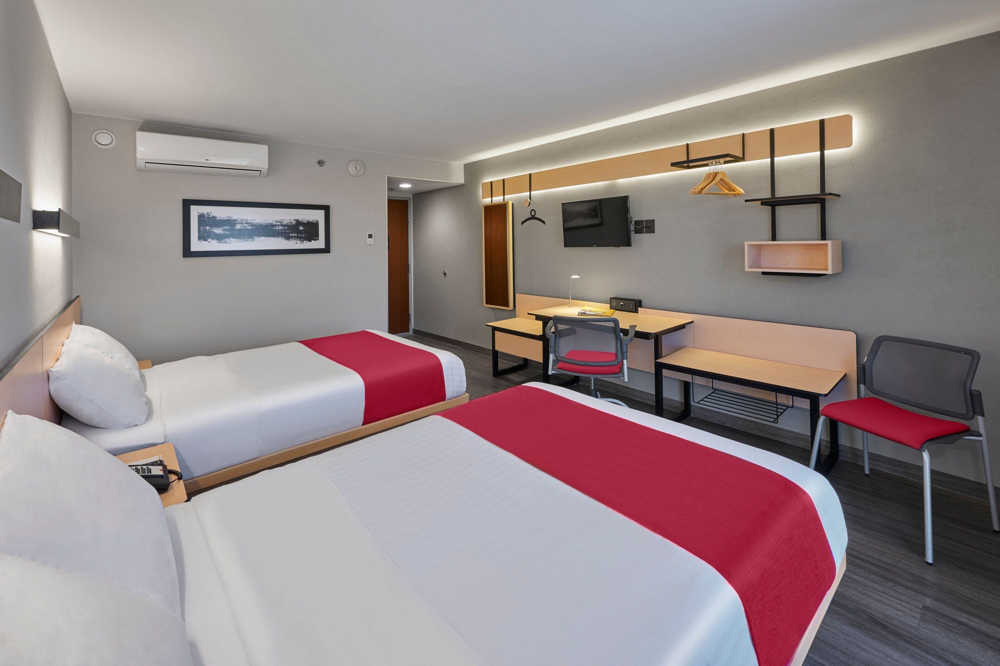 Habitación de hotel con dos camas, un escritorio, una silla, un televisor y un perchero.
