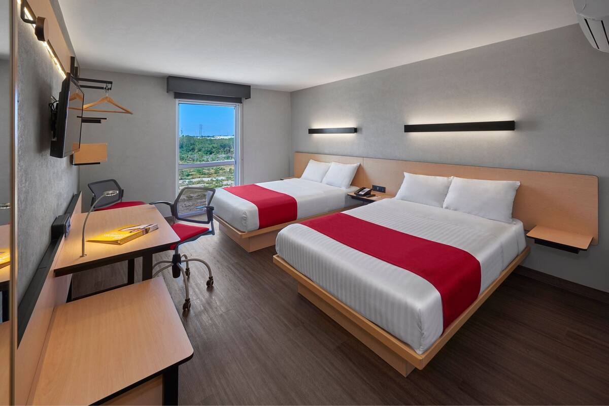 Ein Hotelzimmer mit zwei Betten, einem Schreibtisch, einem Sessel und Blick ins Freie.