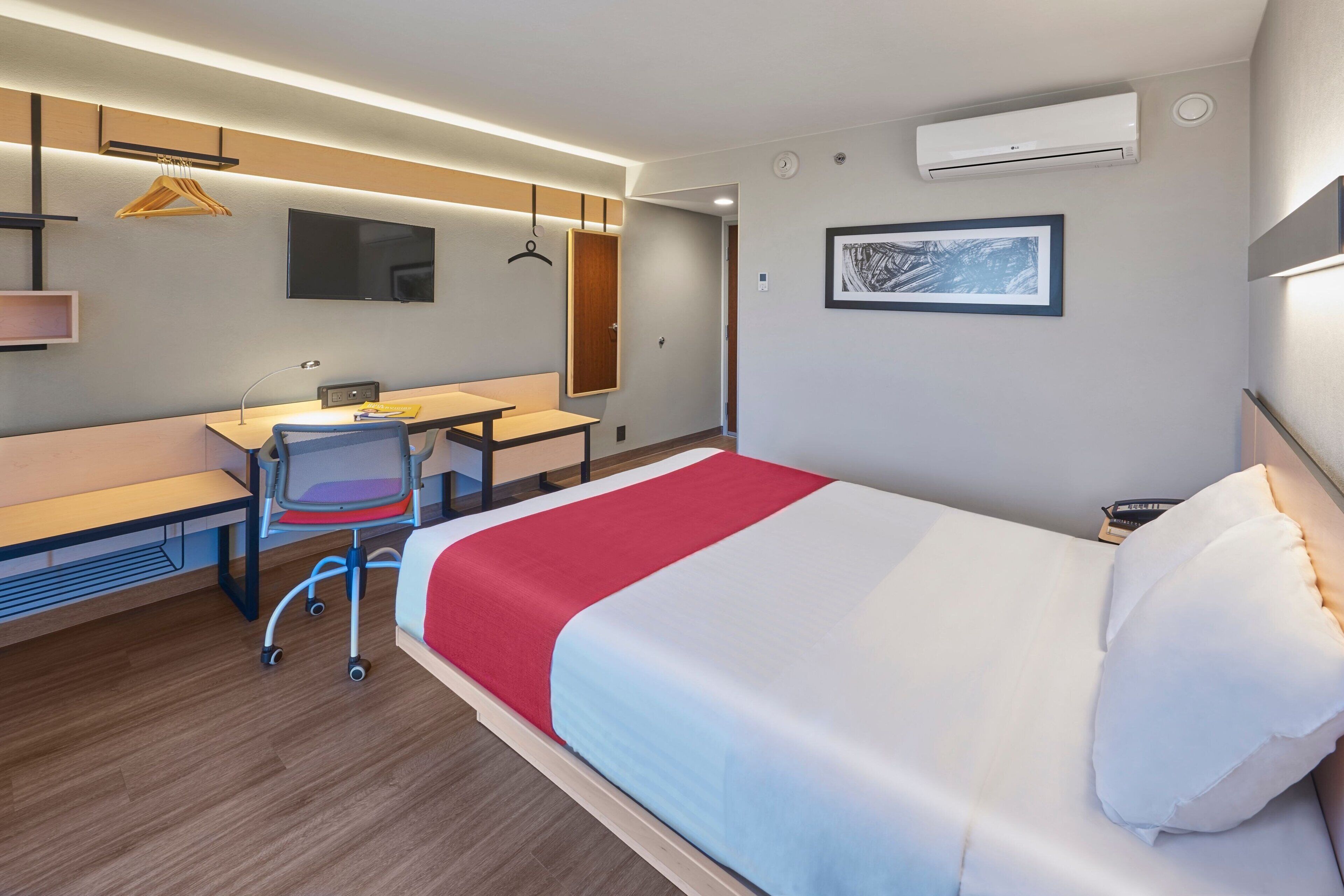 A modern hotel room with a bed, desk, chair, and a TV.