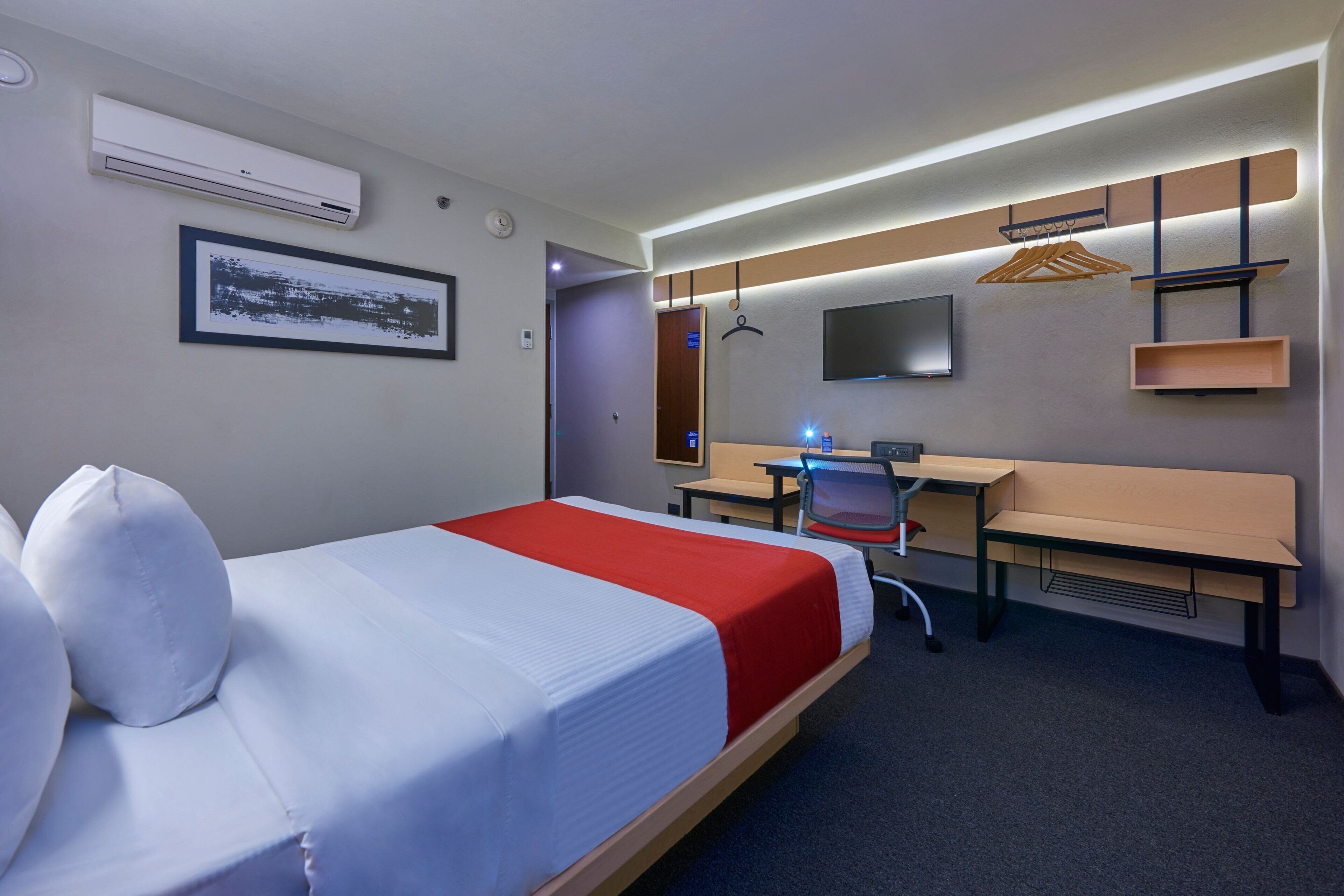 A hotel room with a bed, desk, chair, and a TV mounted on the wall.