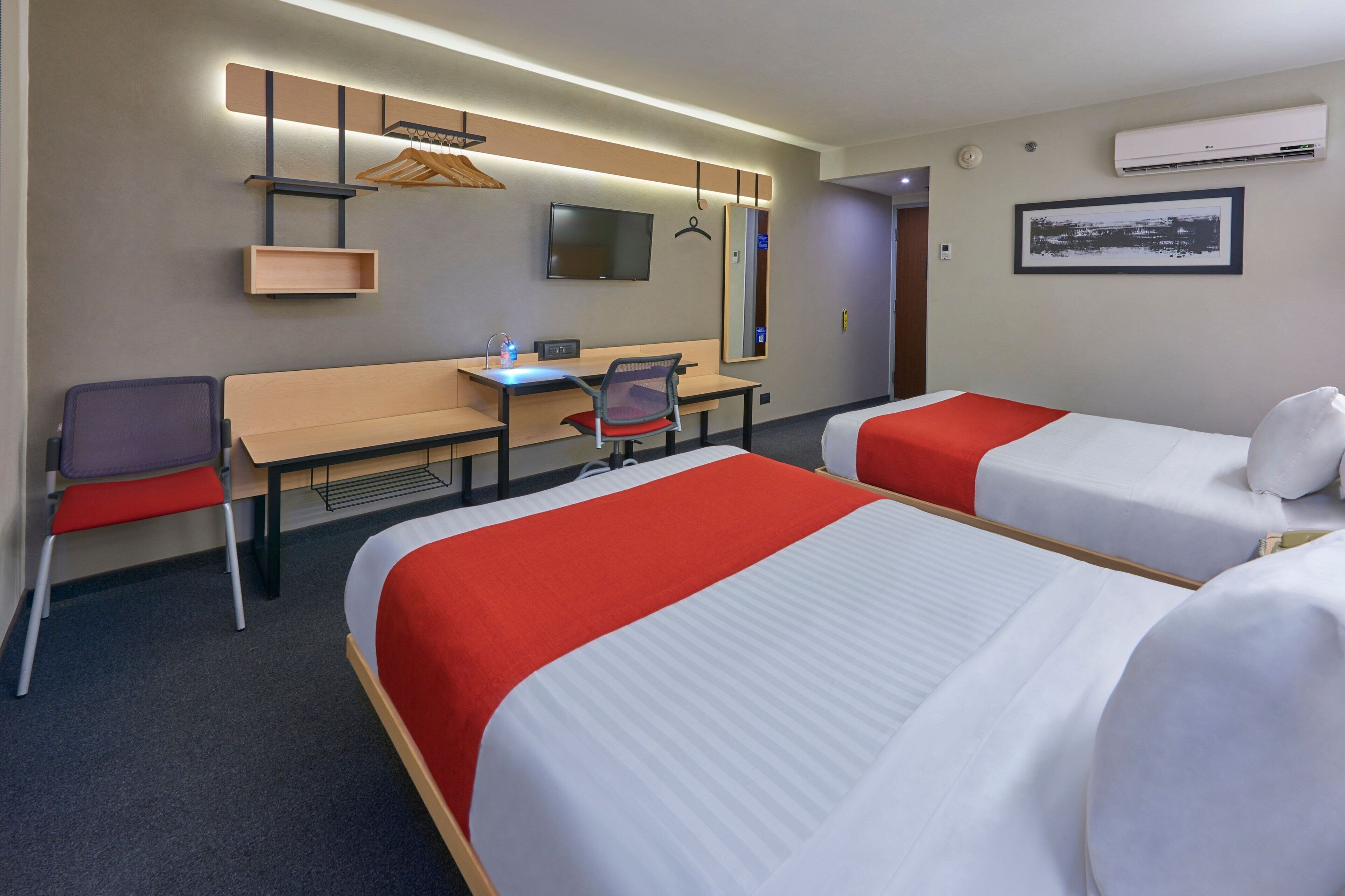 Una habitació d'hotel amb dos llits, una taula, una cadira, un televisor i un armari.