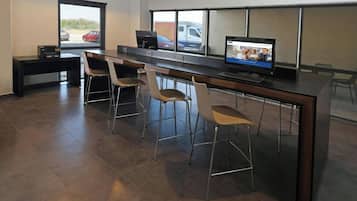 Un espacio de oficina moderno con un escritorio largo, tres sillas, una computadora y una ventana con vista a coches estacionados.