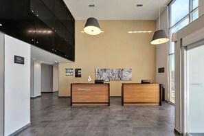 Uma área de recepção com balcão de madeira, duas luminárias pendentes, uma obra de arte emoldurada na parede e uma grande janela que oferece luz natural.