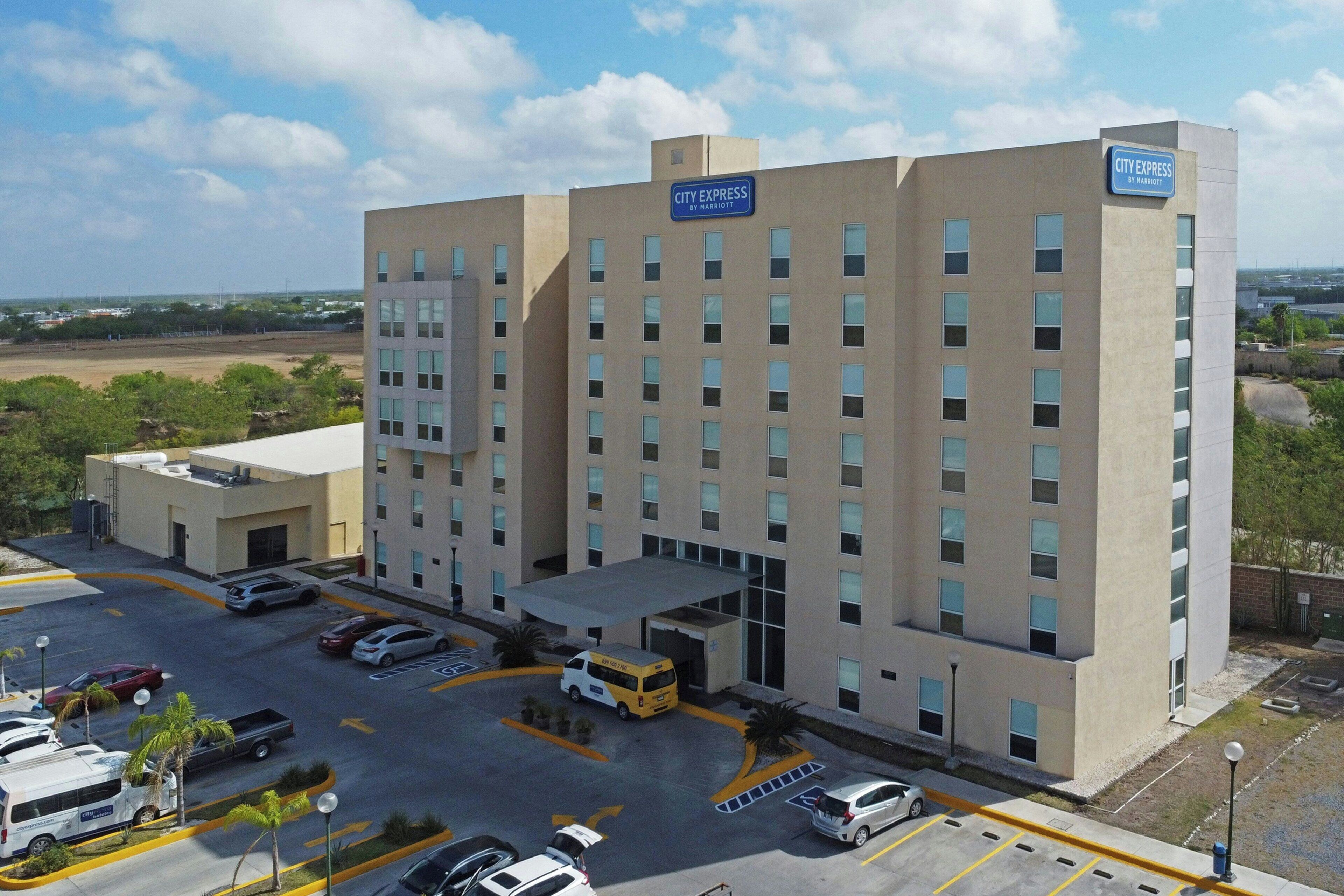 A multi-story hotel with a flat facade, a parking lot with several cars, and a sign indicating it is a Marriott hotel.