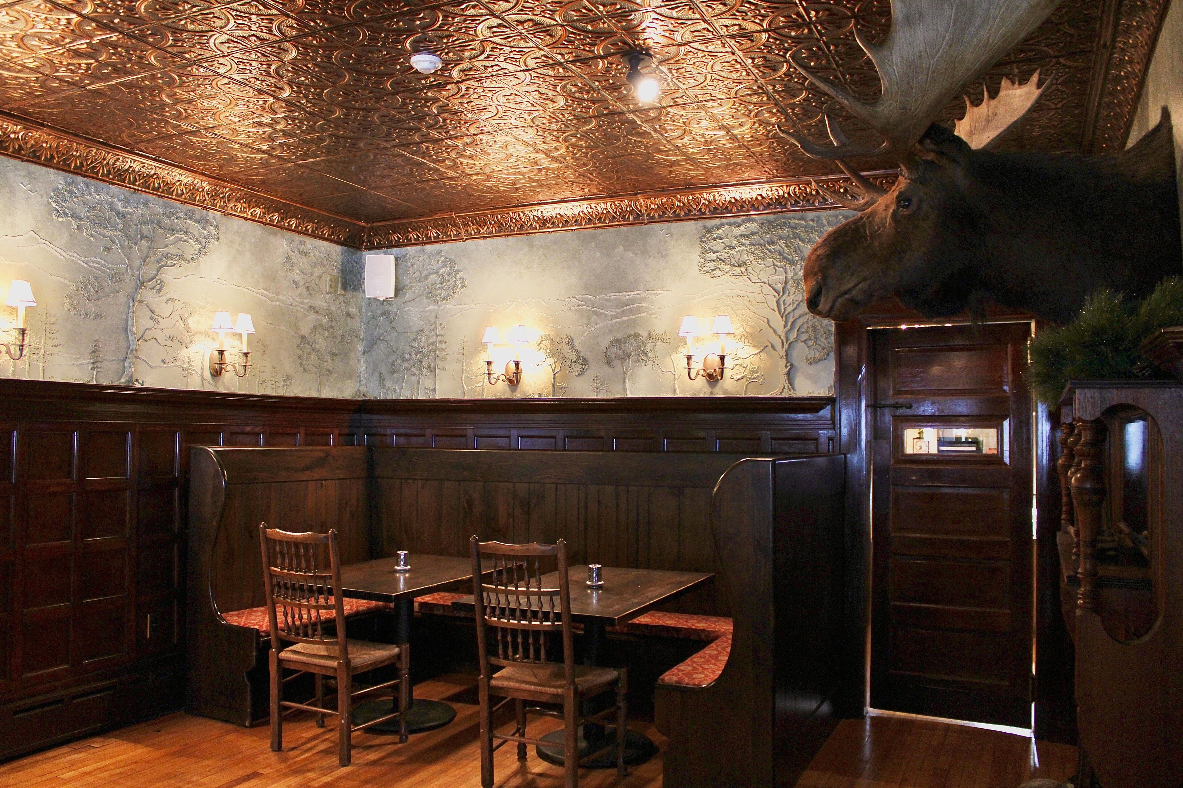 Un restaurante con cabinas de madera, una decoración de cabeza de alce y apliques en la pared.
