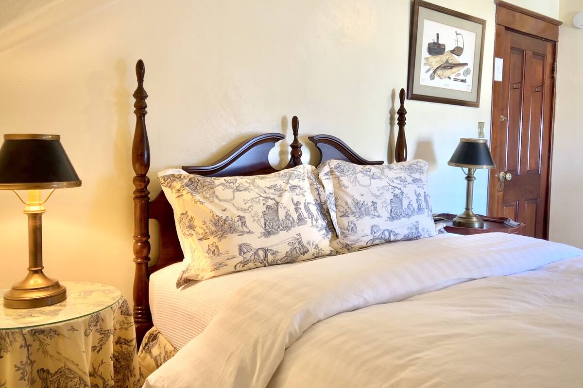 A neatly made bed with patterned pillows, a wooden headboard, and two bedside lamps on round tables.