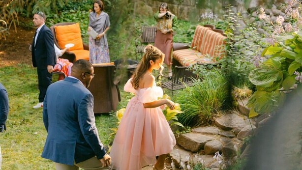 An outdoor garden setting with a stone pathway, seating areas, and lush greenery.