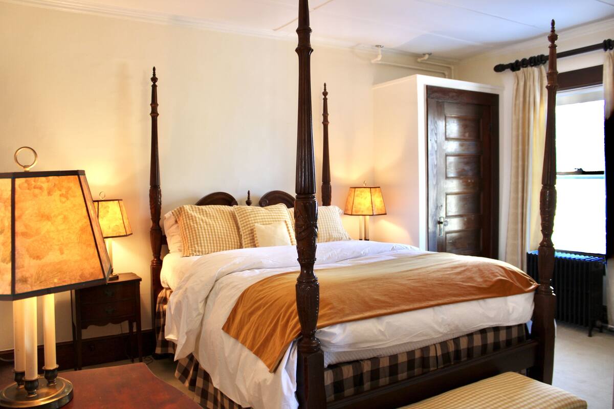 A four-poster bed with a wooden frame, two bedside tables with lamps, and a checkered bedspread.