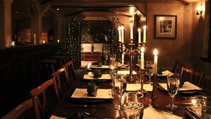 A dimly lit restaurant with candlelit tables, wooden chairs, and a view of the cityscape through a window.