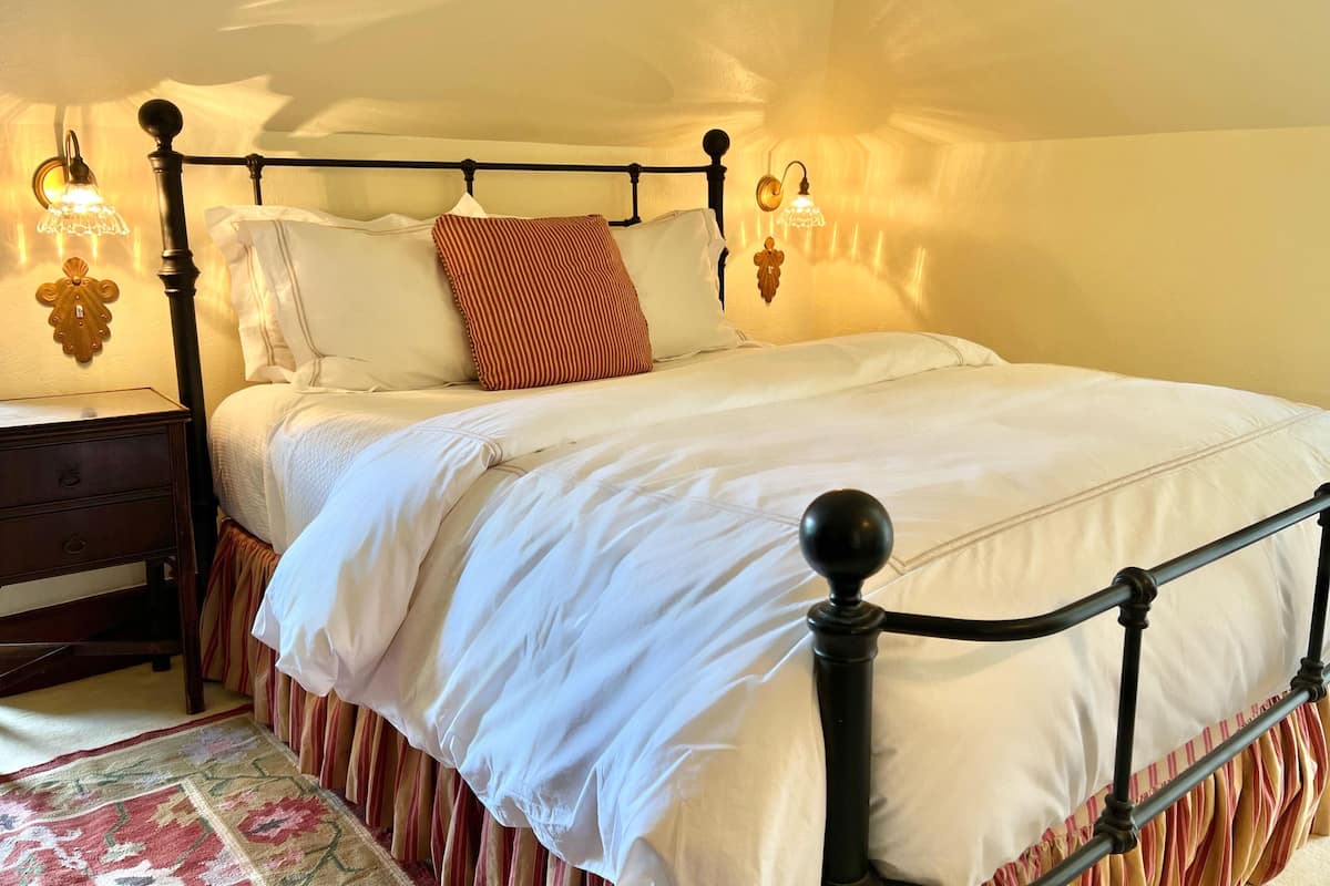 A neatly made bed with a black metal frame, white bedding, and a striped pillow. There are wall sconces with warm lighting on either side of the bed.