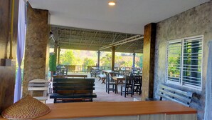 Un espacio al aire libre para comer con bancos y mesas de madera, techo cubierto y vista a zonas verdes.