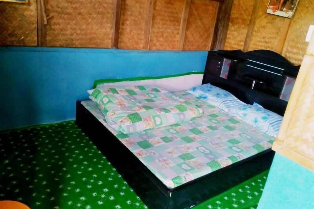 A single bed with a quilt, a wooden headboard, and a green patterned floor.