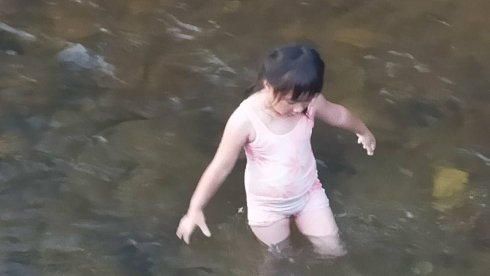 Criança de biquíni rosa brincando em águas rasas.