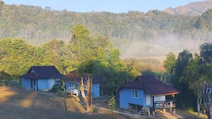 Un entorno rural con dos casas azules, rodeadas de árboles y un paisaje montañoso.