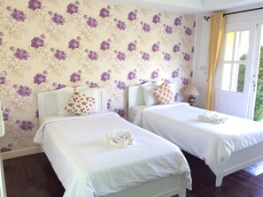 Une chambre avec deux lits, un papier peint à motifs floraux, une fenêtre avec des rideaux et une lampe de chevet.