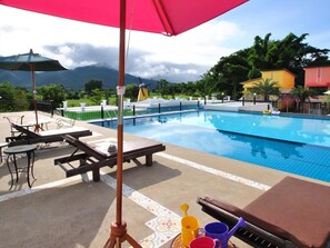 Un espace piscine avec des chaises longues, une table et un parasol rouge.