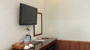 Een hotel receptie met een houten balie, een aan de muur bevestigde televisie, een kleine koelkast en een prullenbak.