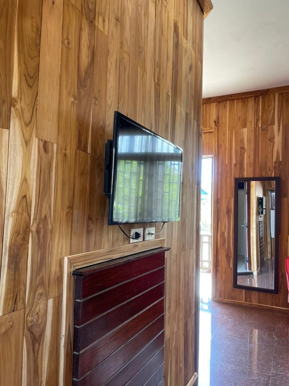 Ein Zimmer mit Holzwandverkleidung, einem an der Wand befestigten Flachbildfernseher und einem Kamin mit rotem Rahmen.