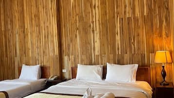 A hotel room with two beds, wooden paneling on the walls, a nightstand with a lamp, and a polished floor.