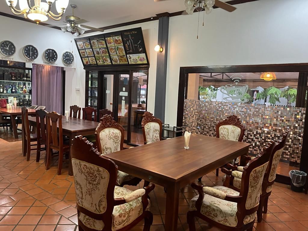 A restaurant interior with a wooden dining table, upholstered chairs, a bar area, and a decorative wall.