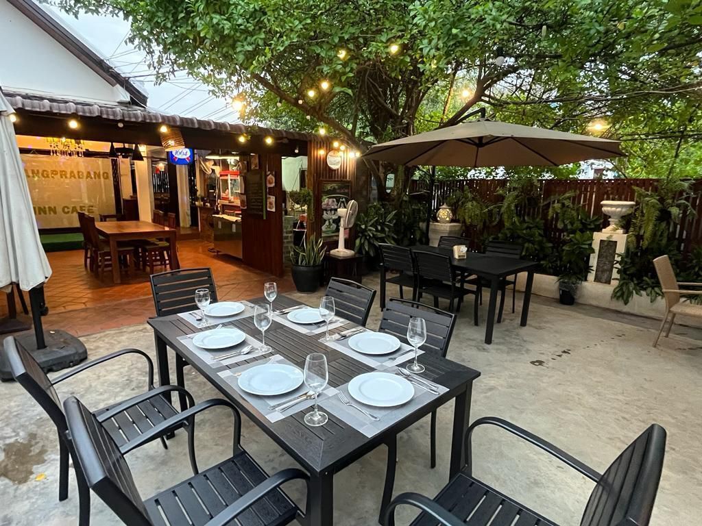 An outdoor dining area with tables set for four, surrounded by chairs and potted plants.