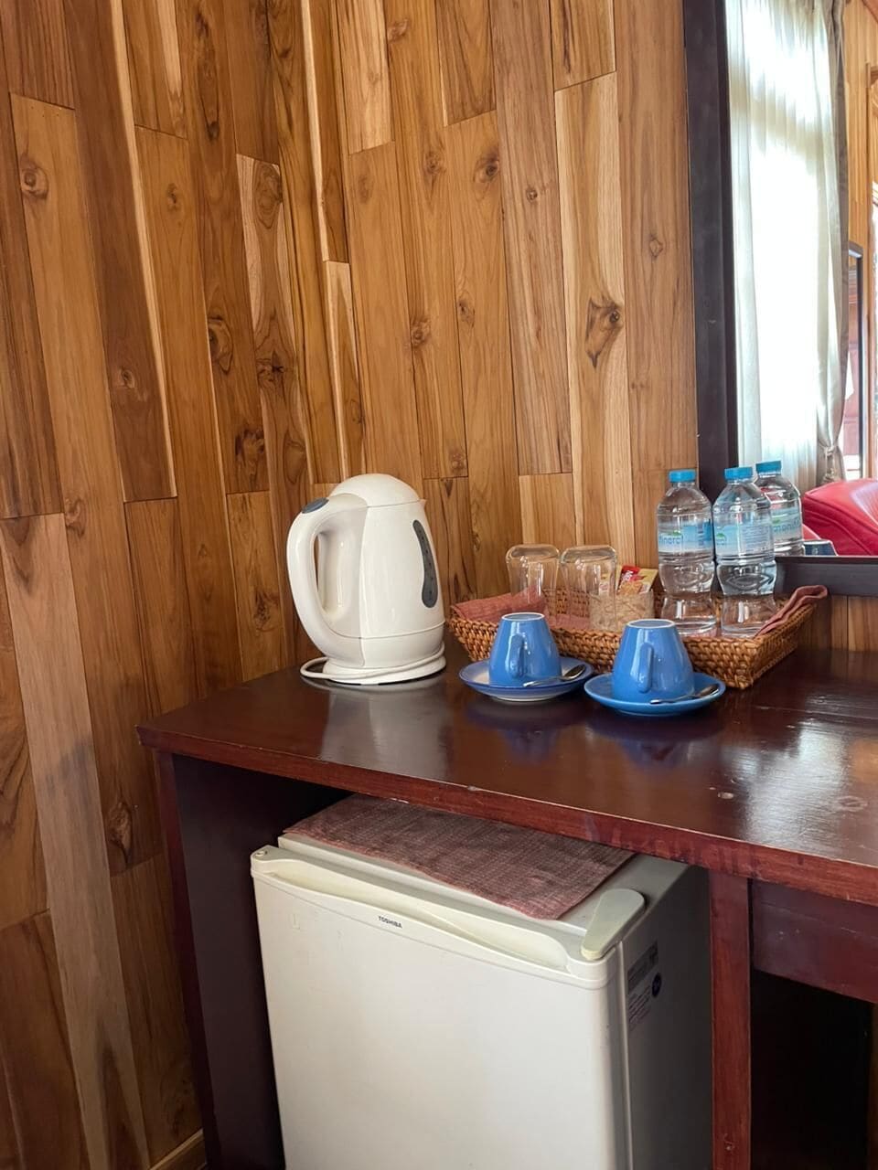 Eine Holzwand, ein weißer Wasserkocher, blaue Tassen und Wasserflaschen auf einem Tisch.