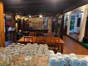 A restaurant interior with a long wooden table, multiple chairs, and a variety of glassware and mugs. - Luang Prabang Inn (Luang Prabang)