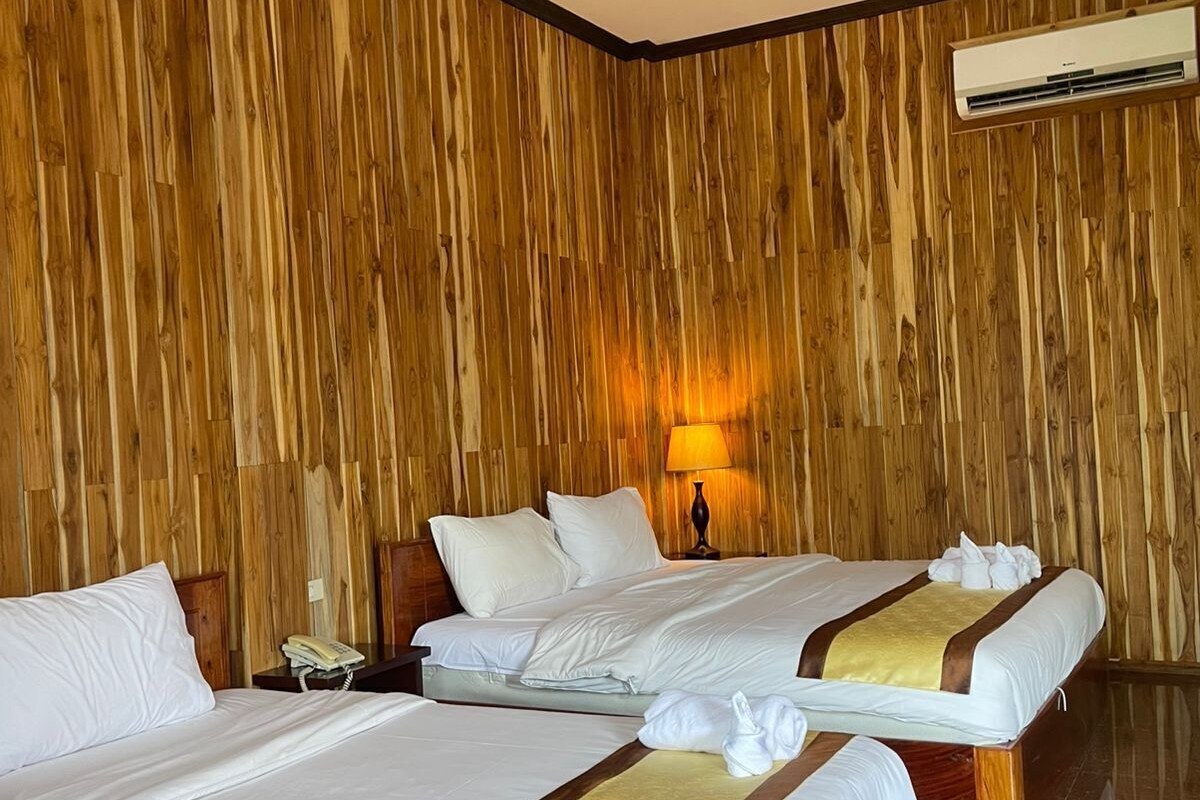 A hotel room with two beds, wooden panel walls, a marble floor, and an air conditioning unit.