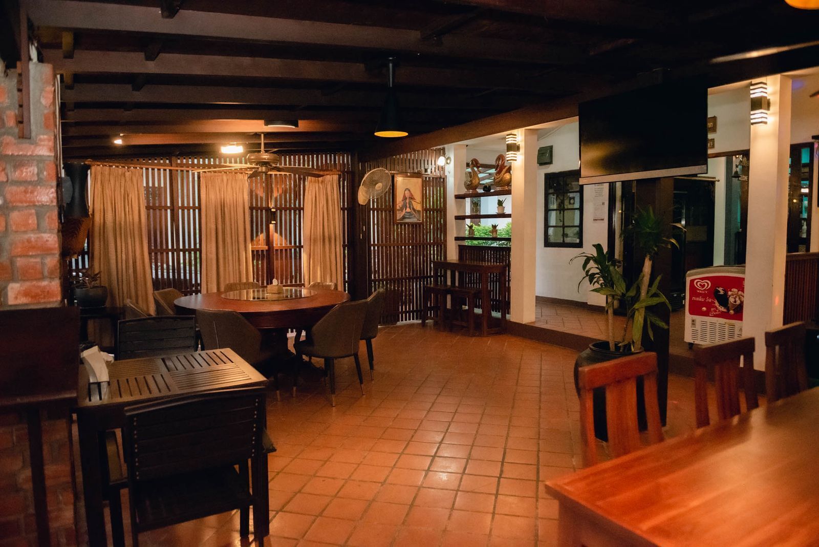 Een restaurantinterieur met een ronde eettafel, stoelen, een bar en een televisiescherm.