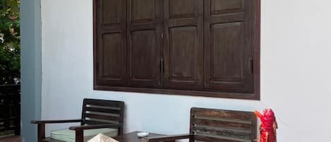 Eine Terrasse mit Holzmöbeln, einem großen Fenster und Topfpflanzen.