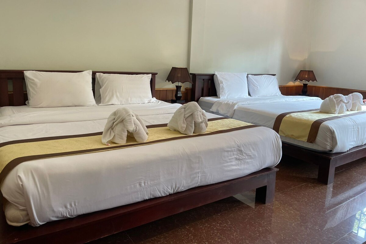 A hotel room with two beds, each with white linens and brown headboards. There are two bedside tables with lamps, and the room has a tiled floor.