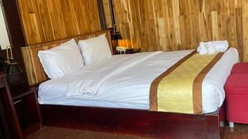 Een hotelkamer met een houten wand, een bed met witte lakens, een nachtkastje met een lamp en een rode stoel.