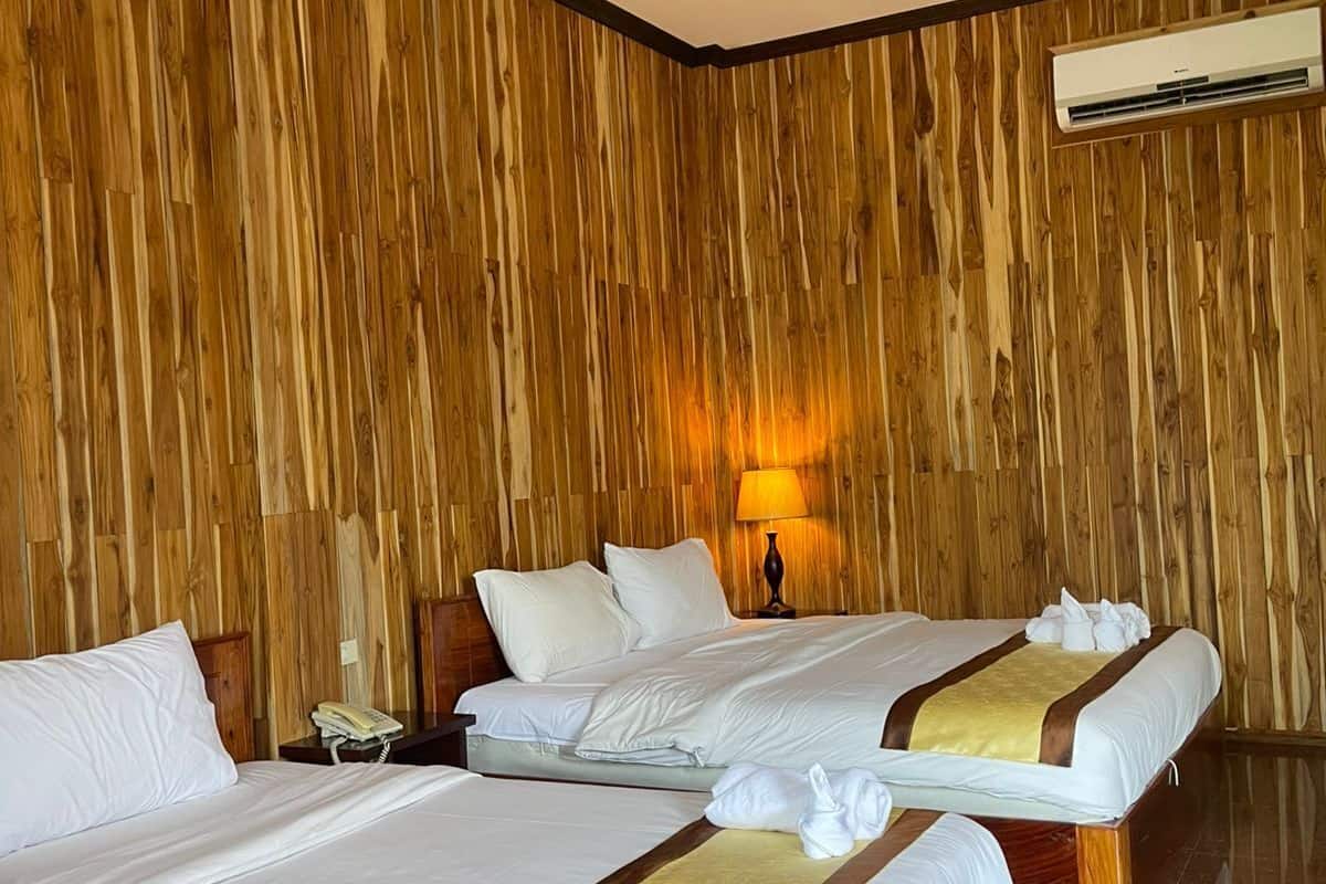 A hotel room with two beds, wooden panel walls, a marble floor, and an air conditioning unit.