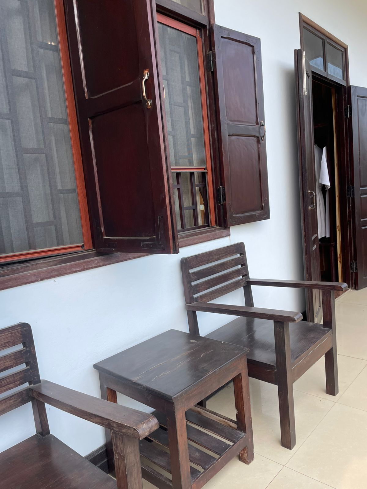 A room with two wooden chairs and a small table, a wooden door with a glass panel, and a window with a wooden frame.