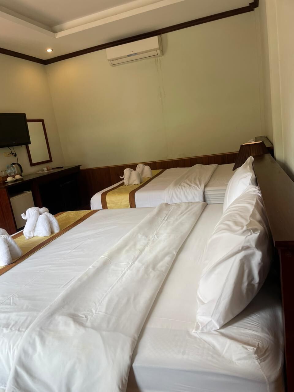 Habitación de hotel con dos camas, un escritorio y un televisor de pantalla plana, además de un equipo de aire acondicionado en la pared.