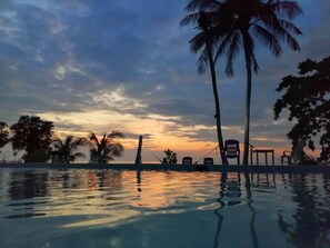 Un área de piscina tranquila con palmeras y sillas de descanso, reflejando el atardecer.