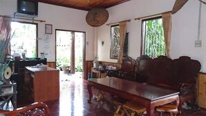 A spacious room with a large wooden dining table, a sofa, and a television mounted on the wall. - Mao Phashok Guesthouse (Luang Prabang)