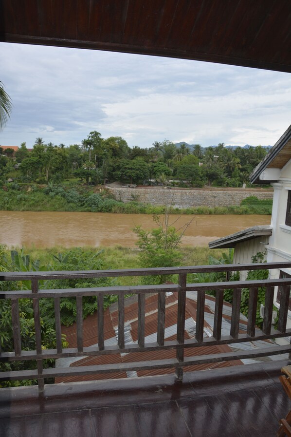 A view from a balcony overlooking a river, with a stone wall and greenery in the background.