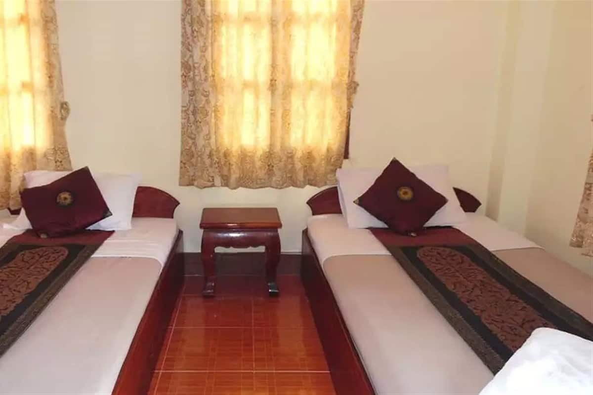 A hotel room with two single beds, a small wooden table, and curtains with a floral pattern.
