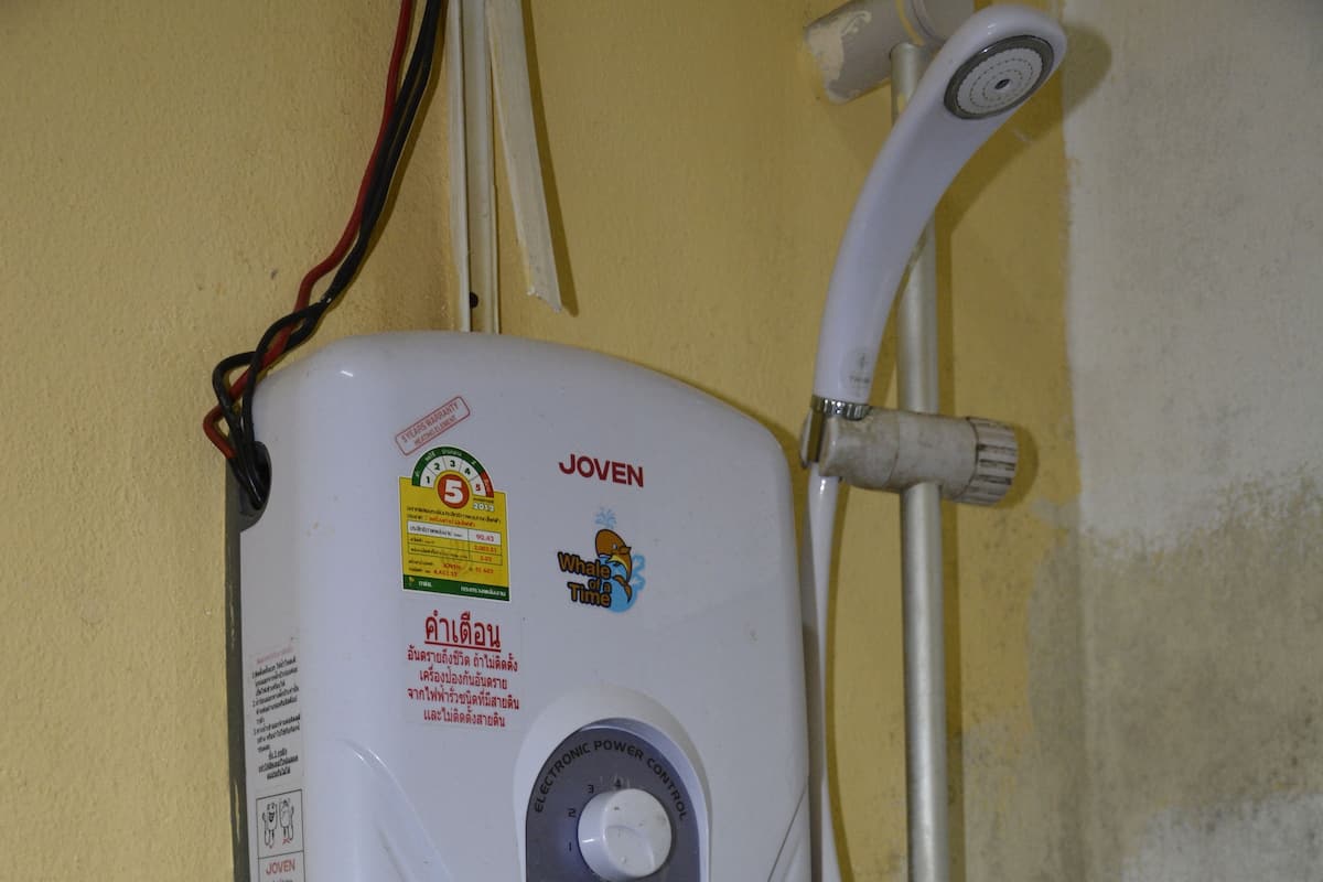 A water heater with a control dial, connected to a showerhead and a hose.