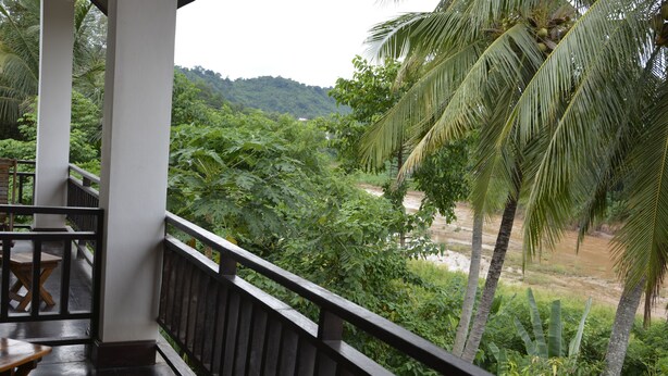 A balcony with a view of lush greenery and a river. - Mao Phashok Guesthouse (Luang Prabang)