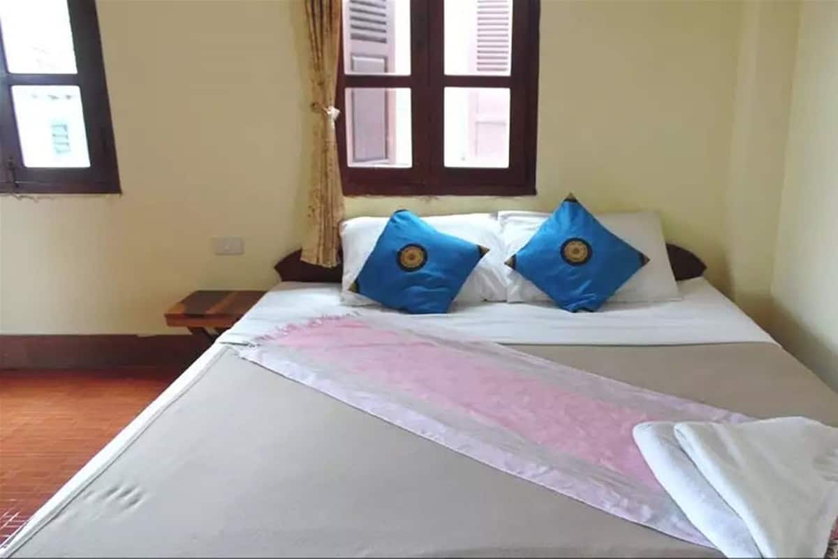 A bed with white bedding, two blue pillows, and a pink blanket.