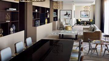 A modern hotel lobby with a long dining table, comfortable seating, and a large bookshelf.