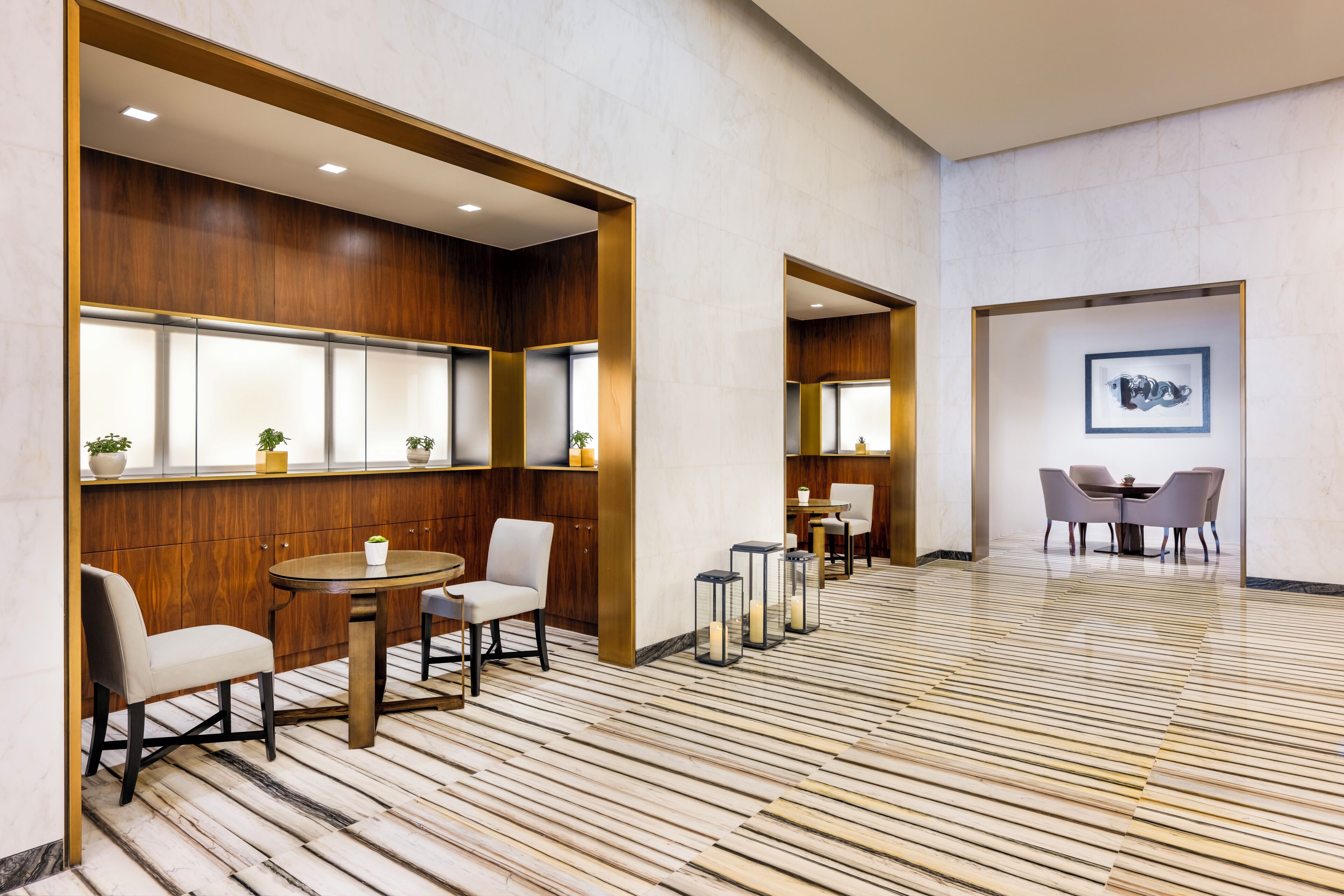 Um hall de hotel moderno com painéis de madeira, piso de mármore e área de estar com mesas e cadeiras.